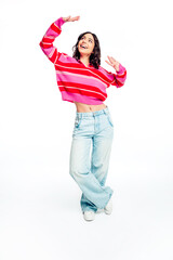 Obraz premium Happy young woman dancing in a pink striped sweater and wide‑leg jeans smiling against a white background