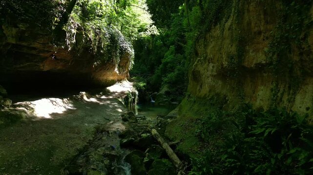 Forest river between mossy rock walls by a cave pool 4k drone