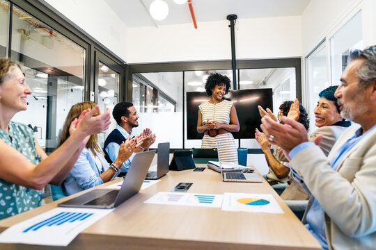 Diverse business professionals applauding smiling woman presenting during a successful corporate meeting in modern office