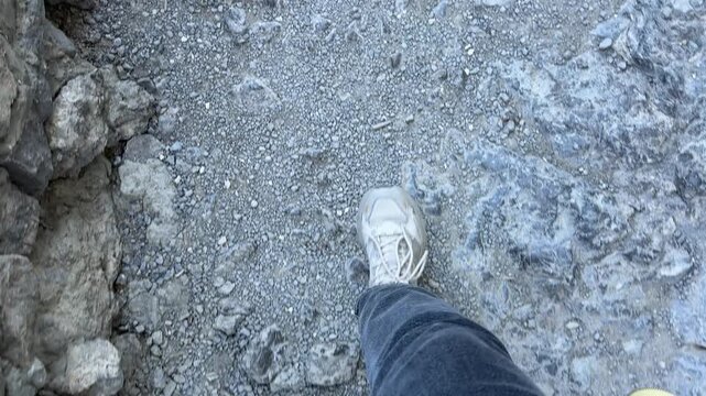 Hiking boots walking, rough rocky mountain trail path outdoors. High angle point of view shot.