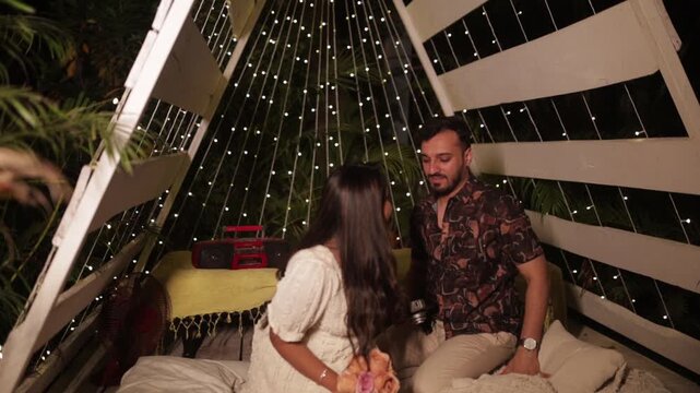 Romantic Couple Exchanging Gift on Cozy Outdoor Date Night Under Fairy Lights