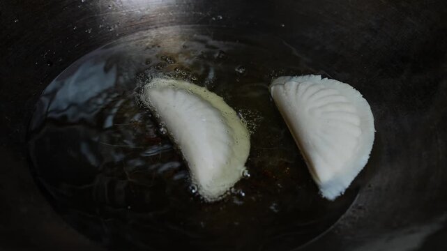 Two dumplings frying in hot oil in a dark pan, close up of homemade food cooking on the stovetop, Dumplings frying in a hot pan