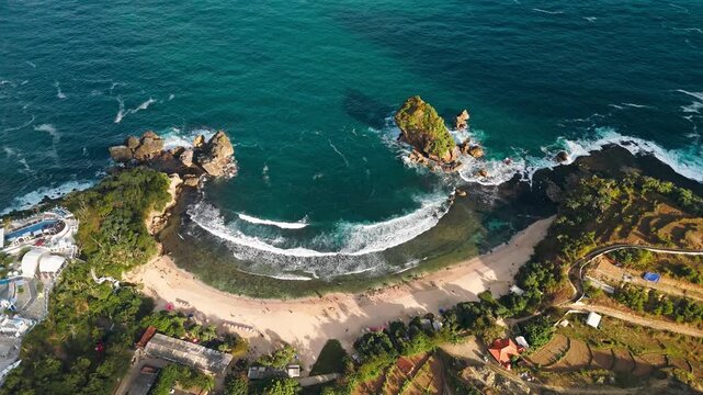 Aerial view of Jungwok Beach with turquoise water, rocky cliffs, and sandy shore in Girisubo, Yogyakarta, Indonesia.