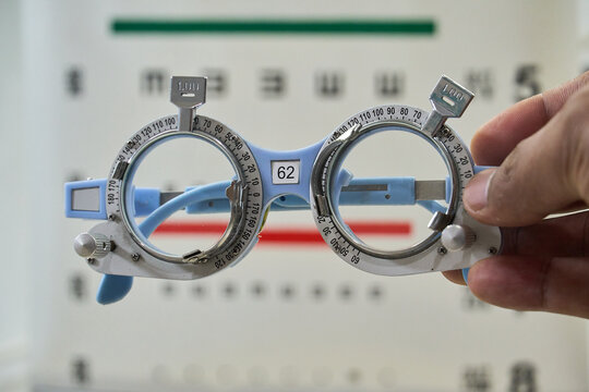 Hand holding optometry trial frame with blurred eye chart background