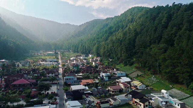 Aerial view of Wisata Bukit Sekipan Tawangmangu nestled in a lush green valley with residential houses and mountain slopes in Kecamatan Tawangmangu, Jawa Tengah, Indonesia.