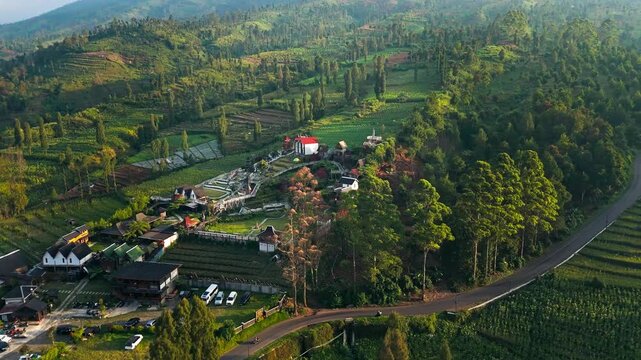 Aerial view of Rest Area Tegal Ombo surrounded by lush green hills, terraced fields, and trees in Kecamatan Candiroto, Jawa Tengah, Indonesia.
