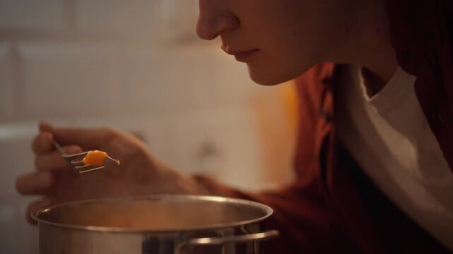 In warm kitchen, man examines doneness of hearty vegetable stew by carefully lifting piece of pumpkin on fork to taste, ensuring vegetables are cooked to perfection. moment highlights cooking process