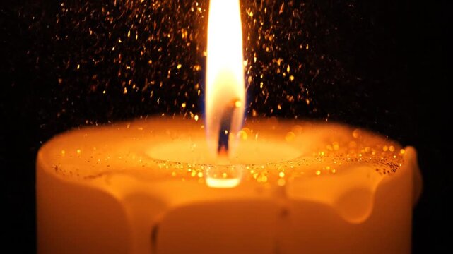 Macro shot of a burning white candle against a black background, featuring a bright flame reflecting in melted wax with golden glitter accents on a wavy liquid surface.