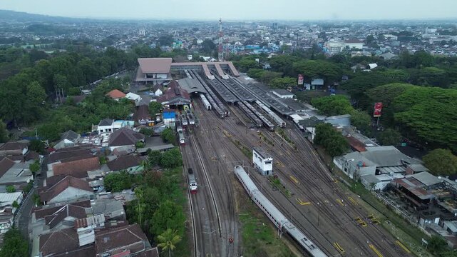 Aerial view of Malang Kota Baru Station with trains on tracks and surrounding urban residential area in Kecamatan Klojen, Jawa Timur, Indonesia.
