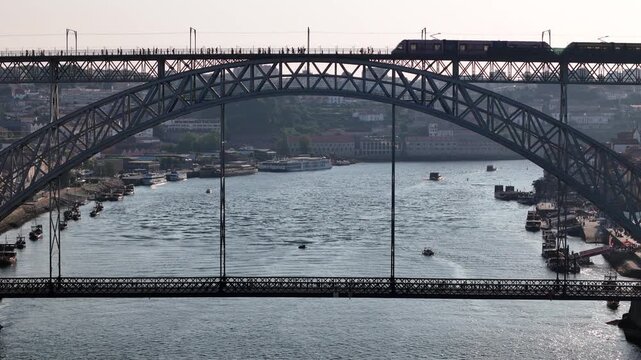 Aerial view of the iconic Luis I Bridge over the Douro River with a metro train crossing the upper deck and boats on the water in Porto, Porto District, Portugal.