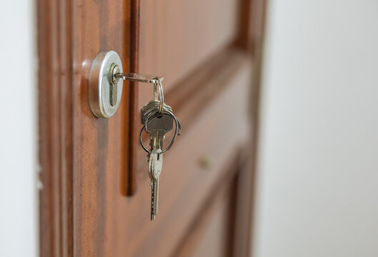 Primer plano de un juego de llaves met&aacute;licas insertado en la cerradura de una puerta principal de madera de color marr&oacute;n, concepto de propiedad o seguridad.