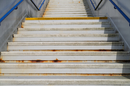 Concrete stairs with blue handrails rise upward during the daytime at the railway station in Forres located in Moray Scotland showing signs of rust
