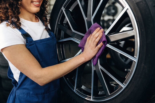 Female auto mechanic cleaning a car wheel with a purple cloth in a garage, showcasing detailed alloy rim and tire in a well-lit workshop environment