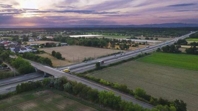 Aerial view of the e-highway test track for trucks with overhead power lines, surrounded by agricultural fields and rural landscape under a sunset sky in Weiterstadt, Hessen, Germany.