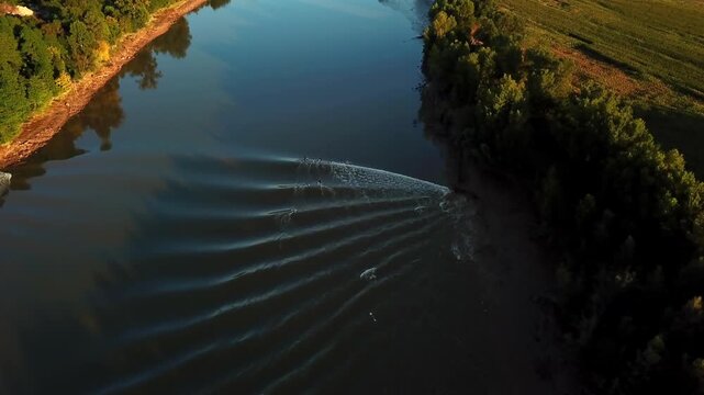 Aerial view of the Mascaret tidal bore wave rolling along the Garonne river near Podensac, with lush trees lining the riverbanks in Mascaret Podensac, Nouvelle-Aquitaine, France.