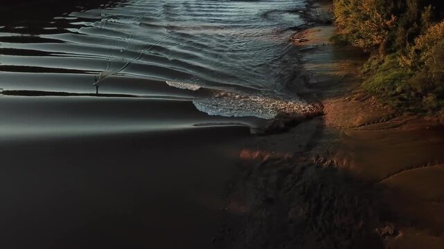 Aerial view of the Mascaret tidal bore wave rolling along the Garonne riverbank at sunset in Mascaret Podensac, Nouvelle-Aquitaine, France.