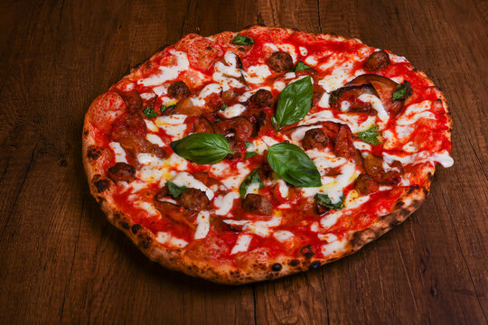 Pizza tradizionale napoletana con sugo di pomodoro, mozzarella, melanzane, polpette fritte e basilico fresco appena sfornata e servita in pizzeria