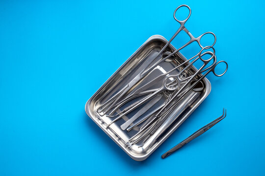 Sterile surgical instruments and tools - scalpels, scissors and others - in a stainless tray on blue background, top view