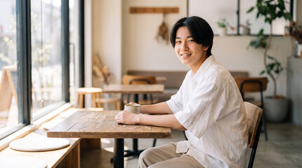 Fototapeta premium 温かみのあるカフェの窓際で爽やかな笑顔を見せる若い男性 ｜ ナチュラル
