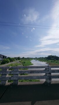 Scenic river flowing beneath a bridge under a blue sky with soft clouds, capturing peaceful tropical landscape, nature, travel destination and beautiful countryside scenery.