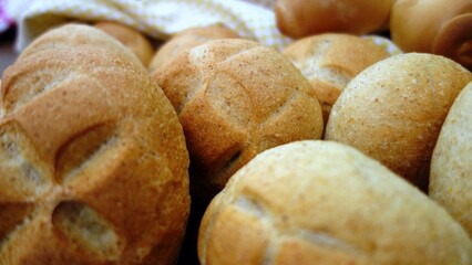 Fototapeta premium Freshly baked artisan bread rolls with a beautiful cross-shaped scoring on top. A close-up view of crusty bread loaves and rolls arranged on a rustic wooden surface, showcasing a variety of baked good