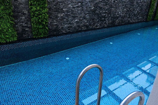 Clean modern pool with blue mosaic tiles and stainless ladder, showing a well-maintained swimming pool interior and water surface.