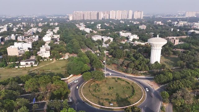 Aerial view of a roundabout surrounded by lush green trees, a prominent water tower, and residential buildings in Greater Noida, Uttar Pradesh, India.