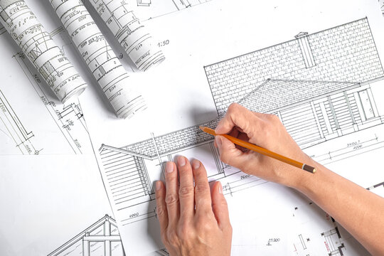 Architect drawing a modern house elevation among blueprints, fabric swatches and material samples, concept of sustainable residential design, renovation planning and interior styling.