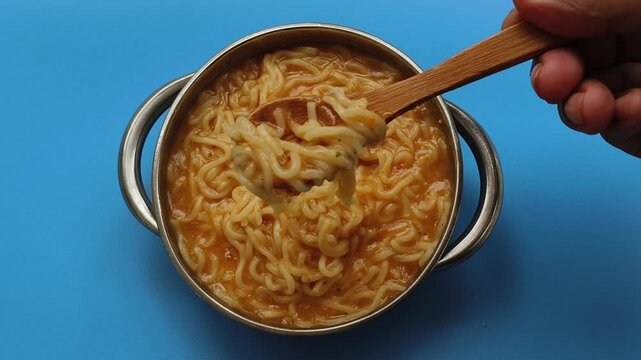Homemade instant noodle or ramen dish inside bowl with spicy flavour ingredients served on table grab using wooden spoon for eating. Closeup of tasty and delicious comfort or fast food.