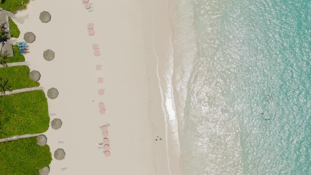 Aerial view of Pink Beach with rows of umbrellas on white sand and turquoise ocean waves in Rock Sound, South Eleuthera, The Bahamas.