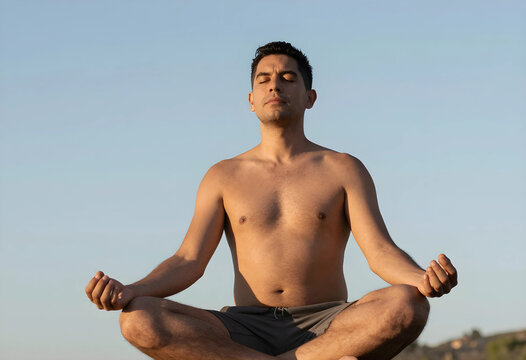 Man meditating outdoors in lotus position with eyes closed, practicing mindfulness and spiritual well being under a clear sky