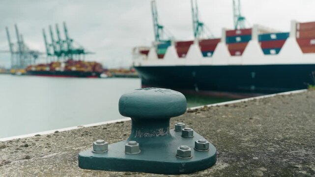 Green mooring bollard with background showing a large container ship entering Deurganckdok Antwerp port - Antwerpen, Belgium