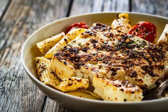 Penne pasta with roasted cherry tomatoes and feta cheese in bowl on wooden table.

