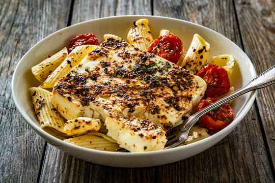 Penne pasta with roasted cherry tomatoes and feta cheese in bowl on wooden table.
