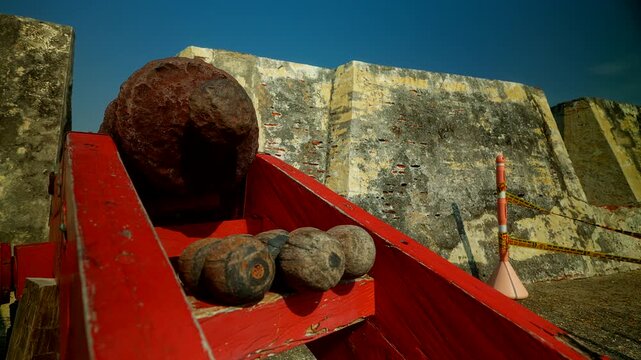 Handheld close-up, historic cannon and cast iron cannonballs at Castillo de San Felipe de Barajas in Cartagena, Colombia, showing preserved colonial military architecture