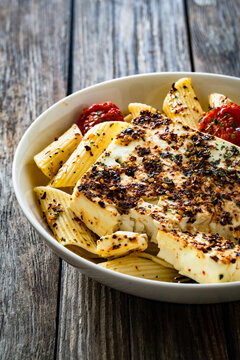 Penne pasta with roasted cherry tomatoes and feta cheese in bowl on wooden table.
