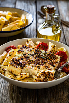 Penne pasta with roasted cherry tomatoes and feta cheese in bowl on wooden table.
