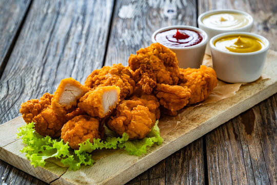 Air fryer breaded chicken nuggets with mayonnaise, ketchup and mustard on wooden table
