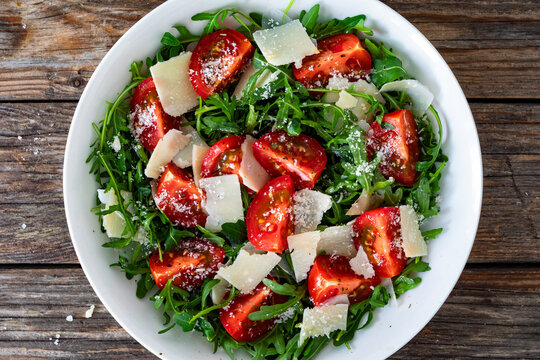 Arugula salad with tomatoes and parmesan cheese on wooden table
