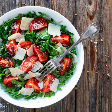 Arugula salad with tomatoes and parmesan cheese on wooden table
