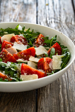 Arugula salad with tomatoes and parmesan cheese on wooden table

