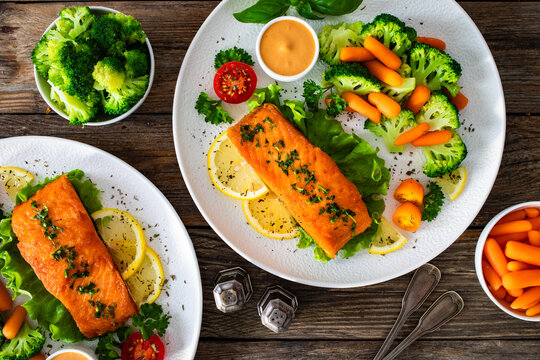 Fried salmon steak with boiled broccoli and mini carrots and mayonnaise on wooden table. Top view
