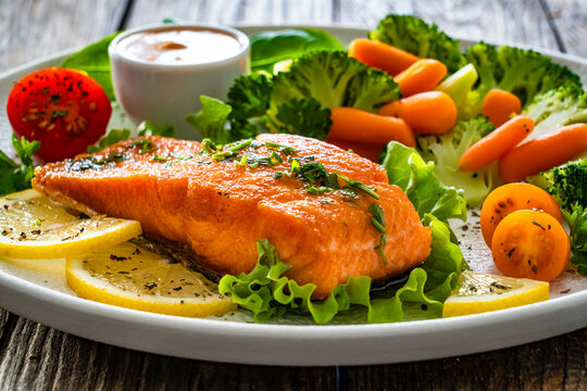 Fried salmon steak with boiled broccoli and mini carrots and mayonnaise on wooden table
