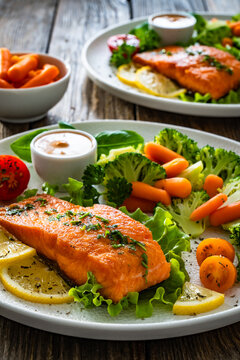 Fried salmon steak with boiled broccoli and mini carrots and mayonnaise on wooden table
