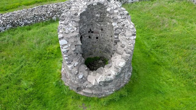 Ruined stone base of an ancient Irish round tower at Nendrum Monastic Site on Mahee Island surrounded by lush green grass overlooking the waters of Strangford Lough