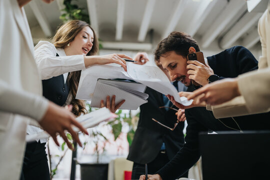 Coworkers rush to exchange documents and sign papers while coordinating over the phone. A hectic office meeting scene showing collaboration, multitasking and deadline-driven teamwork.