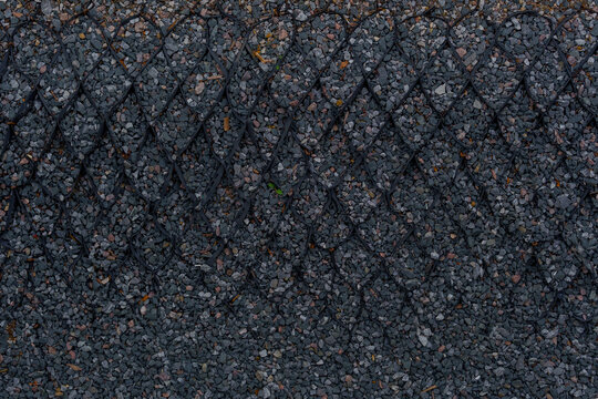 Plastic geocell grid structure filled with dark crushed stone on a construction site. Industrial gravel texture ground layer with cellular mesh for slope stabilization.