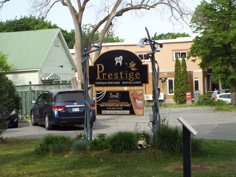 Gatineau, Quebec, Canada &ndash; June 7, 2026: A bilingual "Prestige Clinique Dentaire" sign stands outdoors near a parked blue minivan and buildings along Rue Principale.