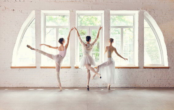 Group ballet dancers performing synchronized jumps in sunlit studio. Concept of dance performance advertising, athletic coordination, artistic expression.