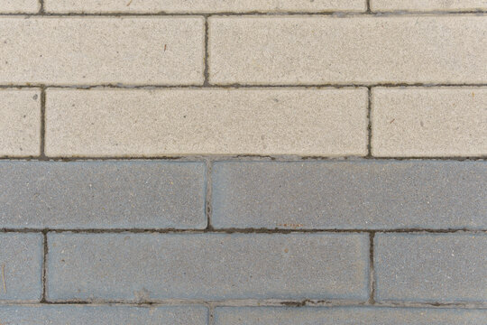 Concrete paving blocks in contrasting light beige and dark grey colors with distinct seam lines. Urban sidewalk stone surface with horizontal brick pattern background.